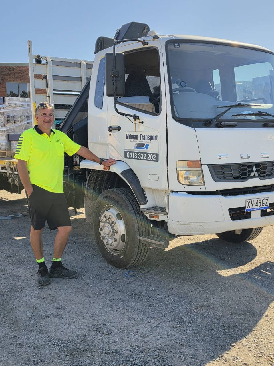 Man standing beside a Milman Transport crane truck at a work site